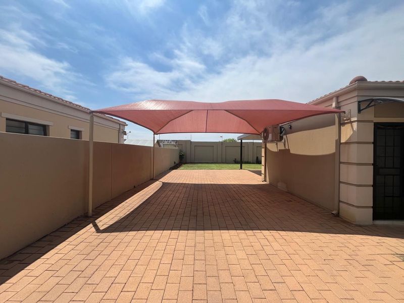 A paved rear courtyard area featuring a large shade sail structure, perimeter boundary walls, and an external air conditioning unit.