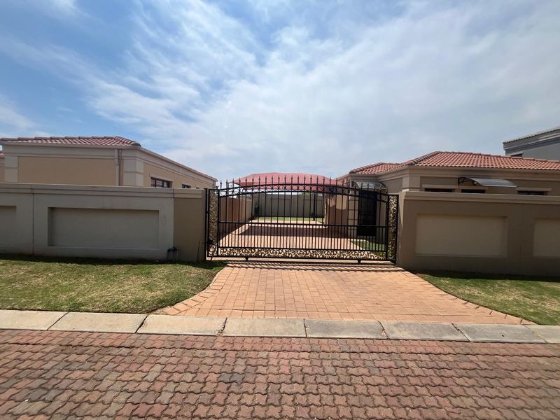 Front view of the property featuring a secure wrought iron gate, paved driveway, and a covered carport area within a walled perimeter.