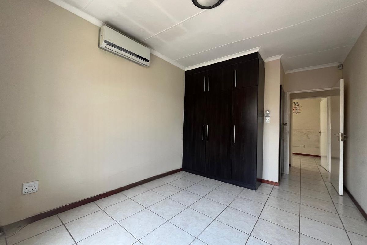 A clean, empty bedroom featuring tiled flooring, a dark wood built-in wardrobe, and a wall-mounted air conditioning unit.