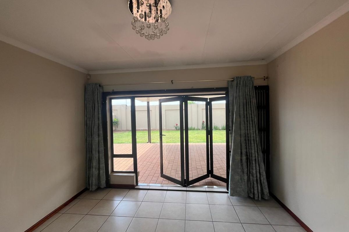 Spacious living area featuring neutral tiled flooring, a decorative crystal chandelier, and large bi-fold doors providing seamless access to the rear patio and garden.