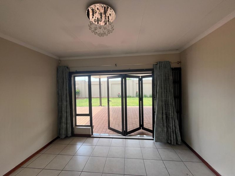 Spacious living area featuring neutral tiled flooring, a decorative crystal chandelier, and large bi-fold doors providing seamless access to the rear patio and garden.
