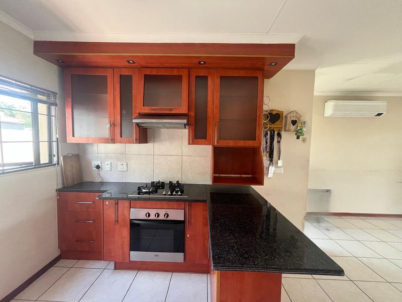 A functional kitchen featuring cherry-wood cabinetry, granite countertops, a built-in oven with gas hob, and tiled flooring, with an adjacent air-conditioned living area.