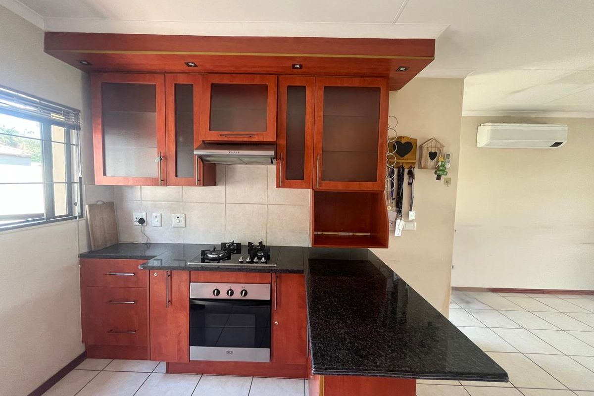 A functional kitchen featuring cherry-wood cabinetry, granite countertops, a built-in oven with gas hob, and tiled flooring, adjacent to an open-plan living area.