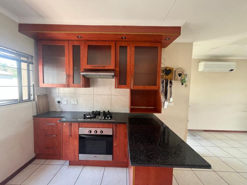 A functional kitchen featuring cherry-wood cabinetry, granite countertops, a built-in oven with gas hob, and tiled flooring, adjacent to an open-plan living area.