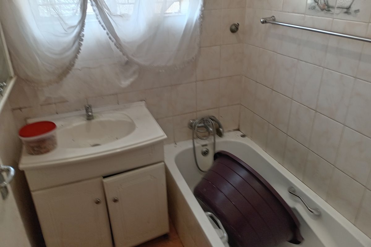 A compact bathroom featuring a built-in bathtub, a vanity basin with storage cabinet, and wall-mounted towel rail.