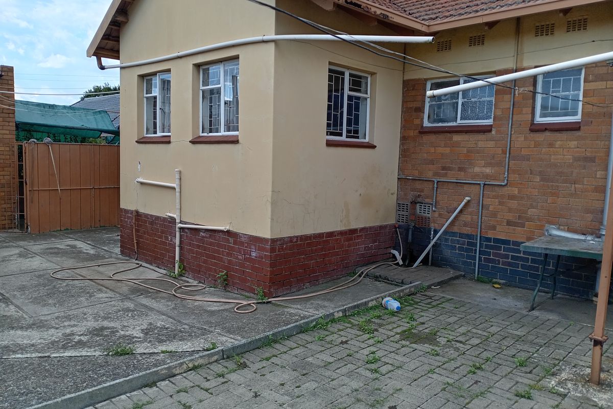 Rear exterior view of the property featuring a combination of plastered and face-brick walls, paved courtyard area, and security-barred windows.