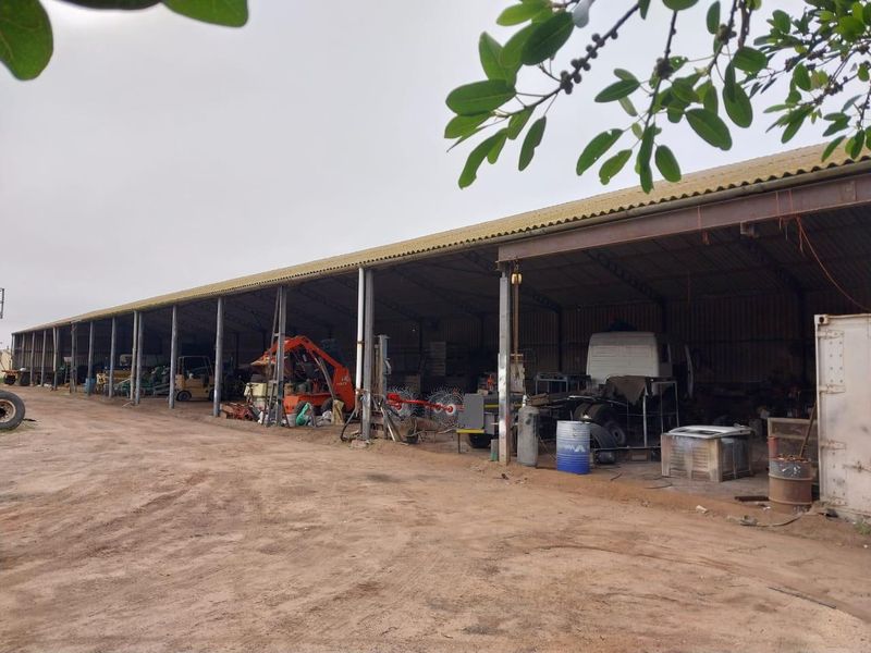 Large open-sided industrial shed with steel frame construction, suitable for agricultural equipment storage or workshop use on a small holding.