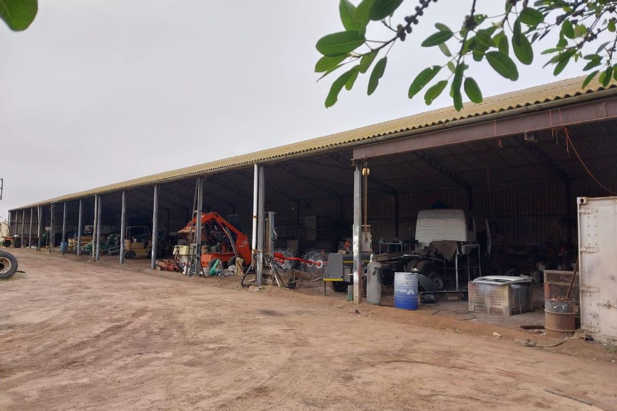 Large open-sided industrial shed with steel frame construction, suitable for agricultural equipment storage or workshop use on a small holding.