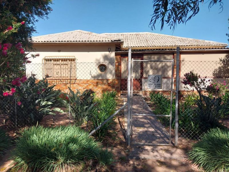 Front view of a single-story residence featuring a tiled roof, brick accents, and a secure gated entrance with established garden landscaping.
