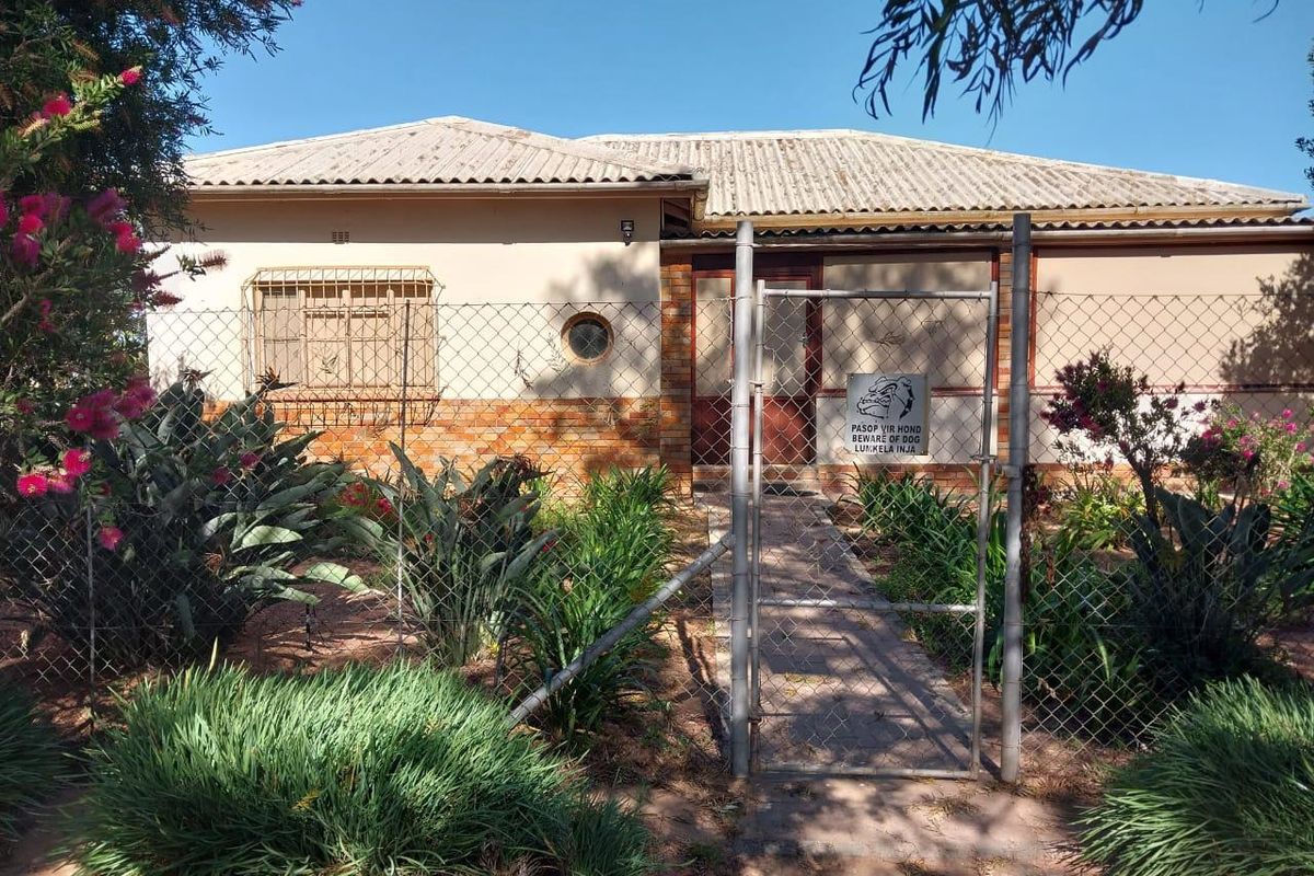 Front view of a single-story residence featuring a tiled roof, brick accents, and a secure gated entrance with established garden landscaping.