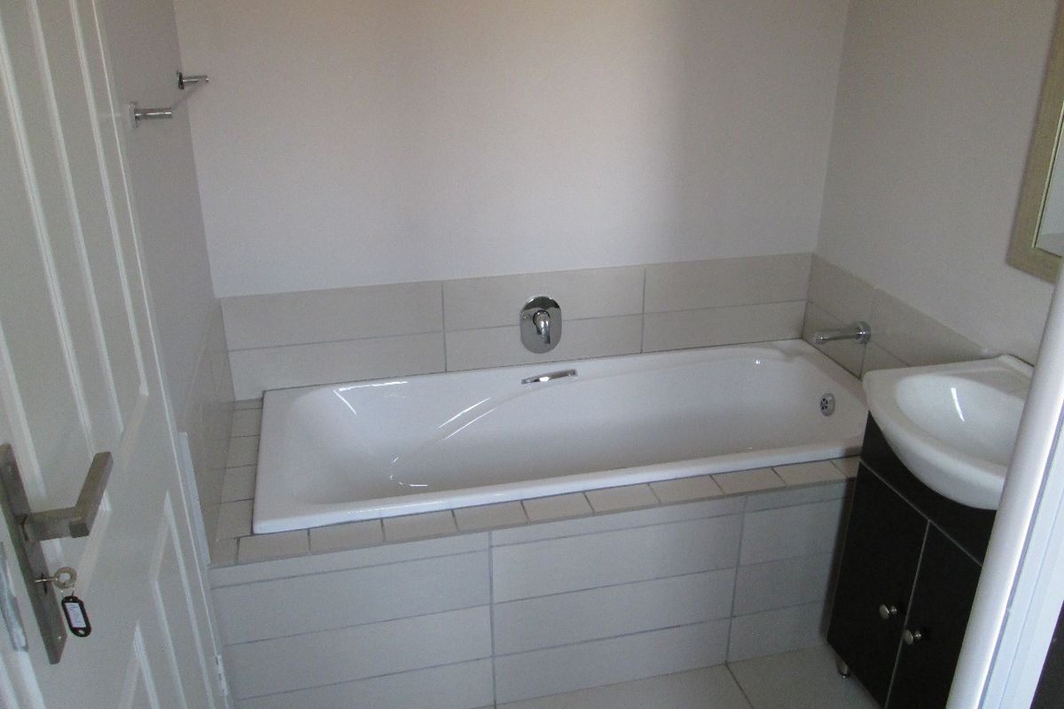 A clean, modern bathroom featuring a built-in bathtub with tiled surround and a vanity cabinet with a basin.