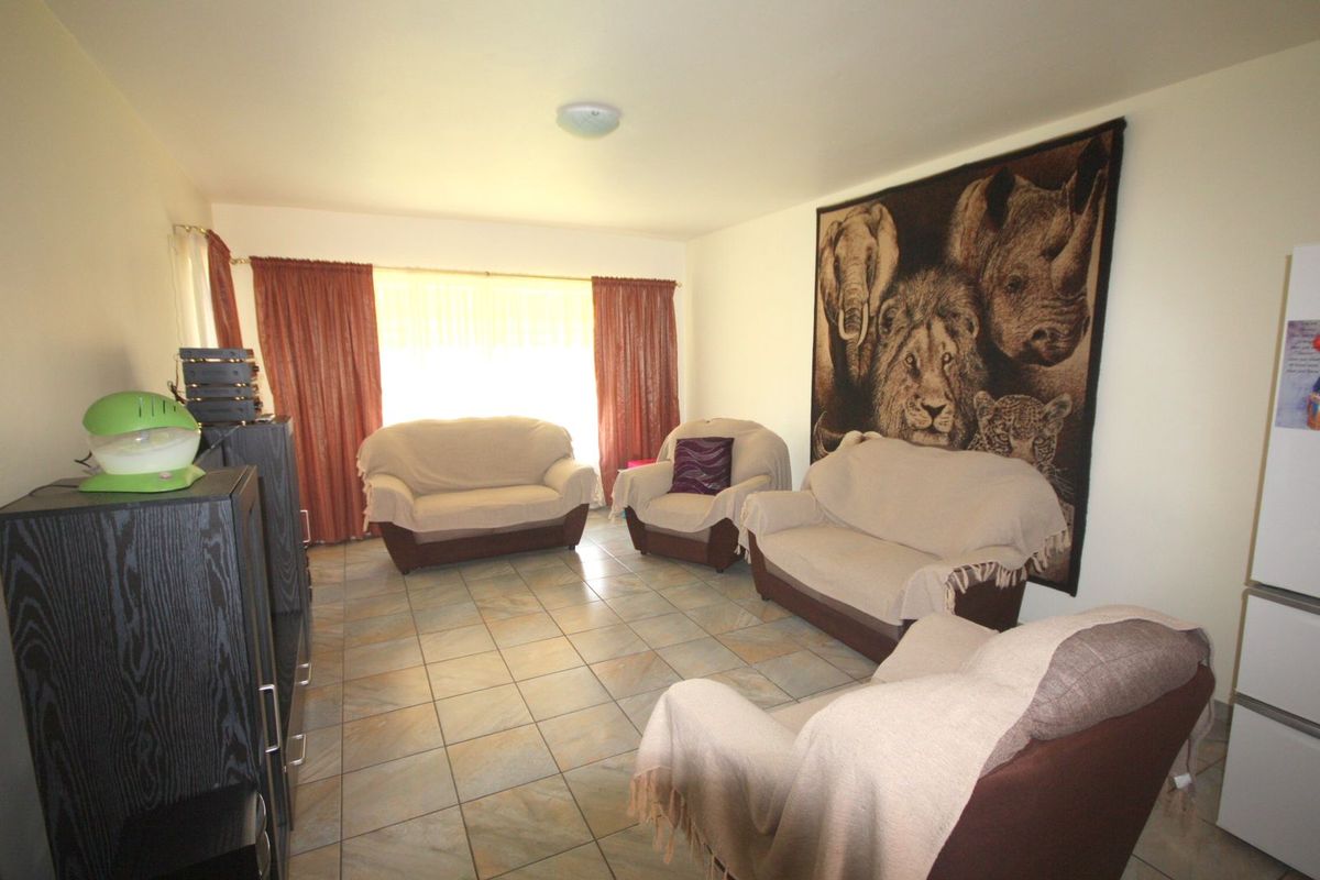 A living room featuring tiled flooring and large windows with curtains, providing a functional and open space for relaxation.