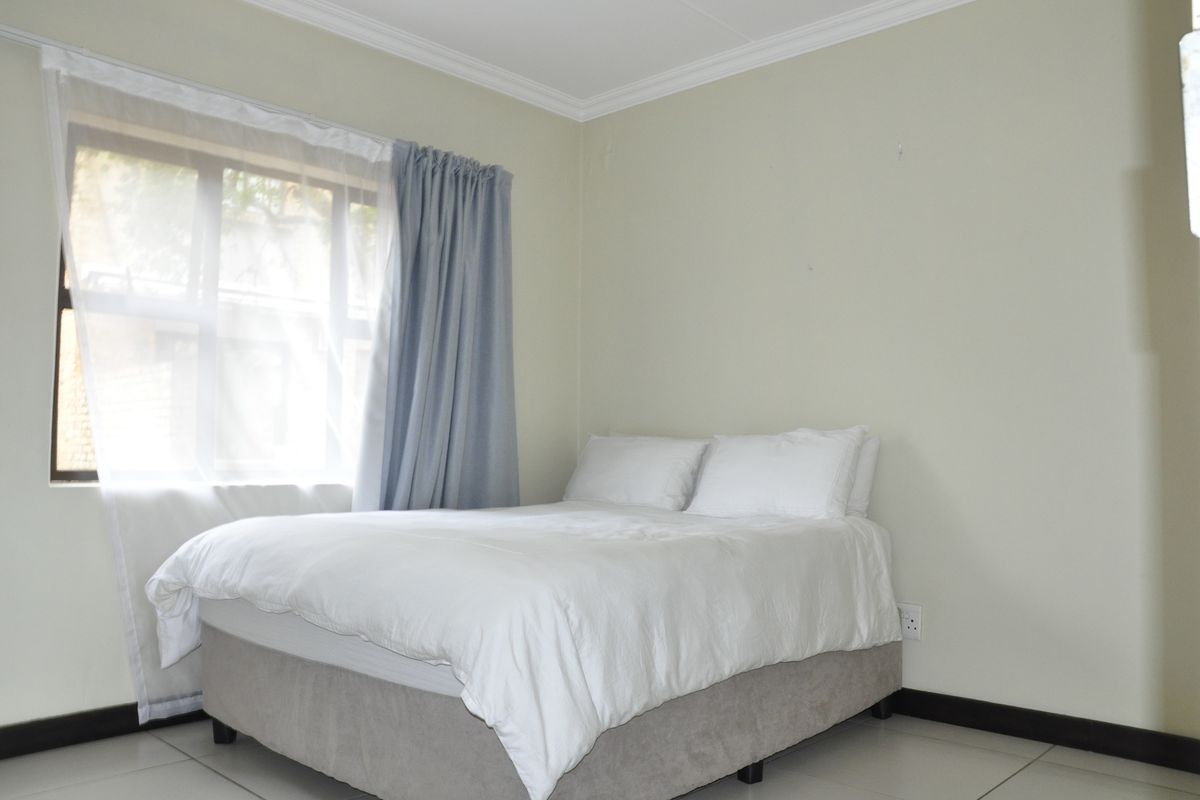 A bright bedroom featuring tiled flooring, crown molding, and a window with natural light.