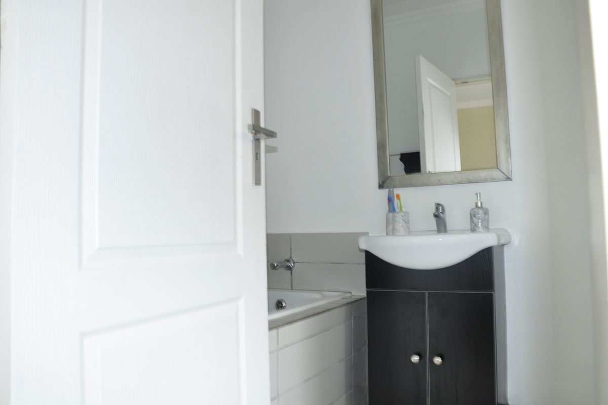 A compact bathroom featuring a modern vanity cabinet with a basin and a tiled bathtub surround.