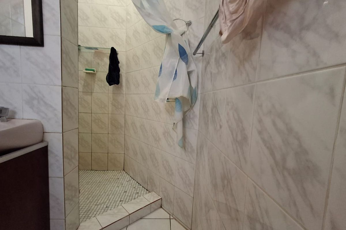A functional bathroom featuring a tiled shower enclosure, vanity basin, and wall-mounted towel rail with neutral marble-effect wall tiling.