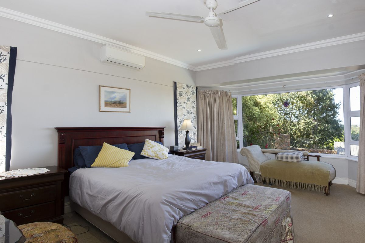 Spacious bedroom featuring a large bay window with garden views, ceiling fan, and wall-mounted air conditioning unit.