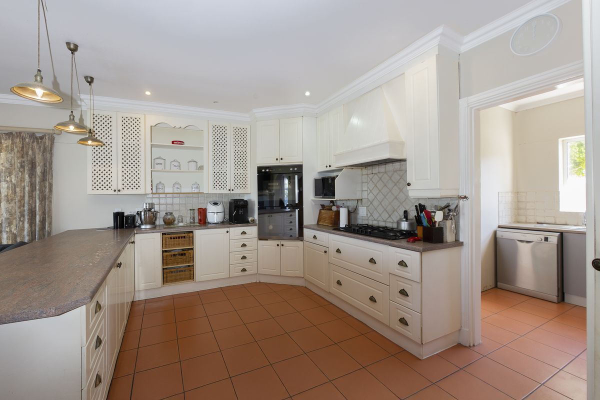 A spacious kitchen featuring classic white cabinetry, gas hob, built-in oven, and tiled flooring, with an adjacent scullery area visible through the doorway.