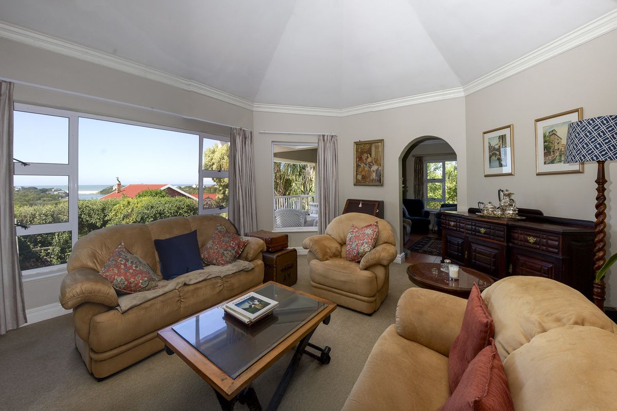 Spacious living room featuring a vaulted ceiling, crown molding, and large windows offering scenic coastal views, with an arched entryway to adjacent spaces.
