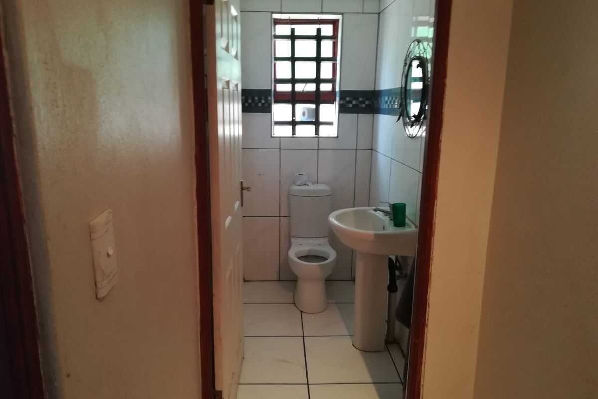 A compact bathroom featuring a pedestal basin, toilet, and tiled finishes throughout, requiring some maintenance and cosmetic updates.
