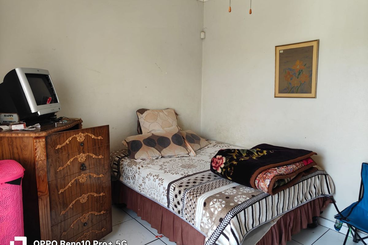A compact bedroom featuring tiled flooring and plain walls, currently furnished with a bed and storage unit.