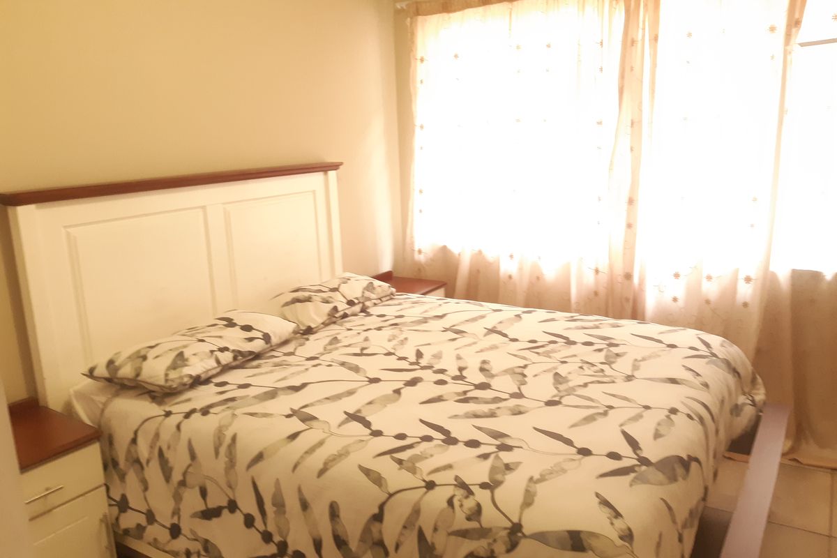 A bedroom featuring built-in headboard and bedside cabinetry with tiled flooring and natural light through window curtains.