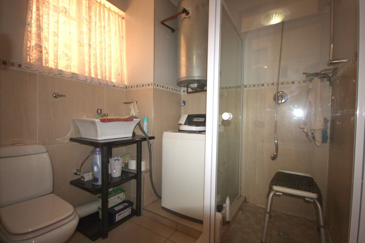 A compact bathroom featuring a shower enclosure, toilet, and integrated laundry area with an exposed water heater.