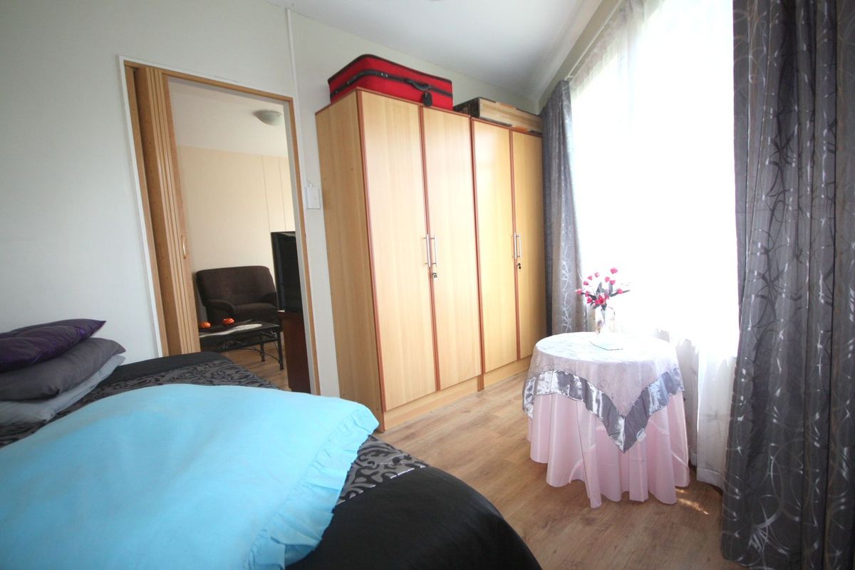 A bedroom featuring built-in wooden wardrobes and laminate flooring, with natural light entering through a large window.