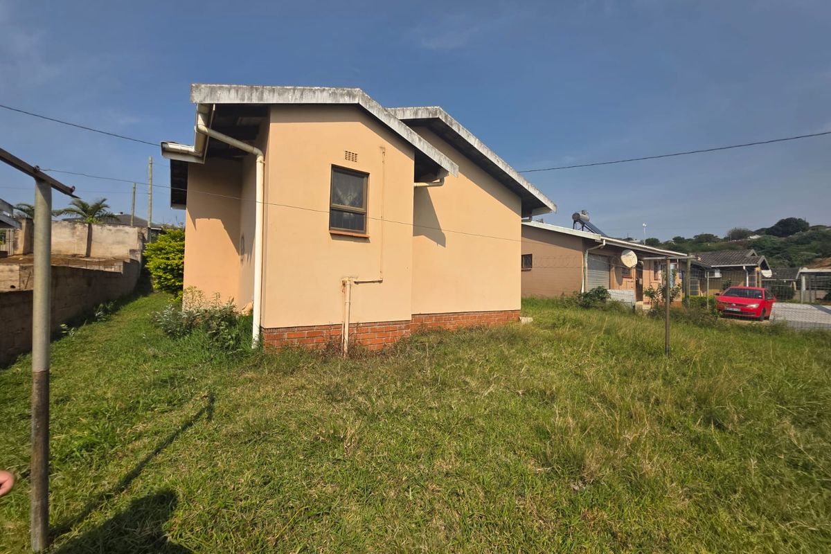 Rear view of the property showing the exterior wall, brick plinth, and surrounding garden area with a solar water heater visible on the roof.