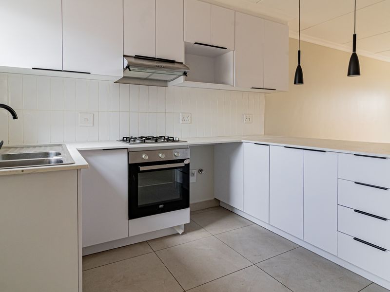 Modern kitchen featuring white cabinetry, stone countertops, gas hob, built-in oven, and sleek pendant lighting in a clean, minimalist layout.