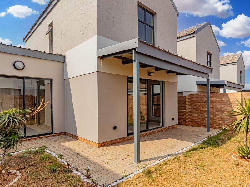 Rear view of the townhouse featuring a covered paved patio, sliding glass doors, and a private garden area with brick boundary walls.