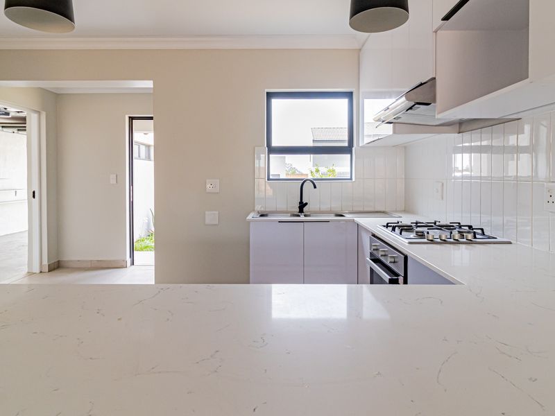 Modern kitchen featuring sleek white cabinetry, quartz countertops, a gas hob, built-in oven, and a clean subway tile backsplash.