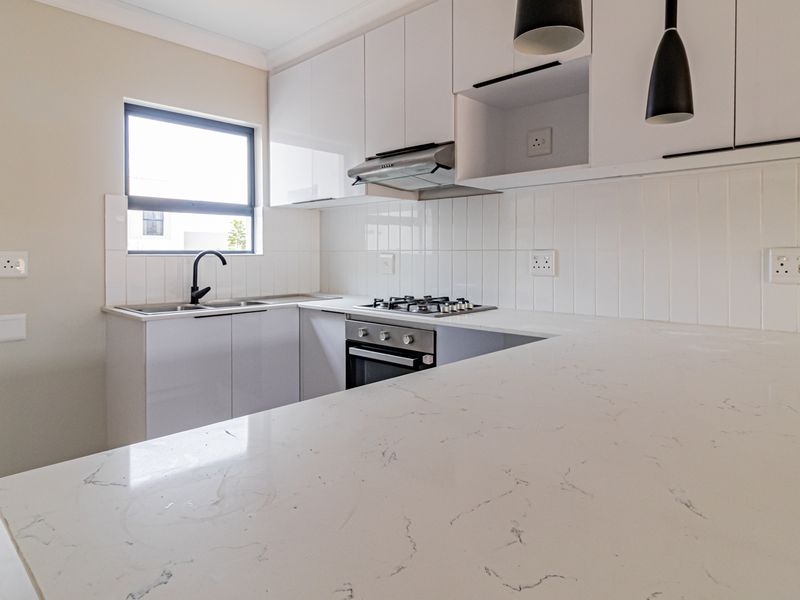 Modern kitchen featuring white gloss cabinetry, stone countertops, a gas hob, built-in oven, and a clean subway tile backsplash.