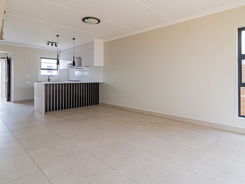 A bright, modern open-plan living and kitchen area featuring neutral tiled flooring, contemporary cabinetry, and clean finishes throughout.