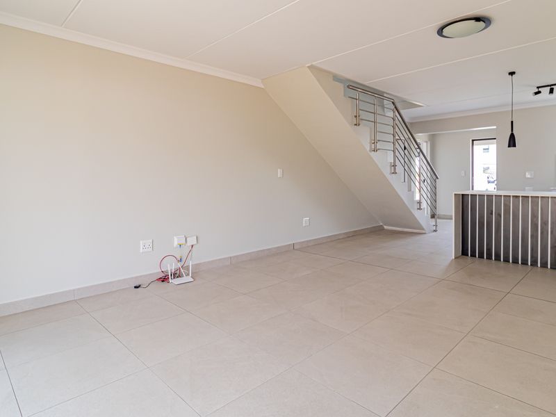 Spacious open-plan living area featuring tiled floors, a modern staircase with stainless steel balustrade, and a kitchen island with pendant lighting.