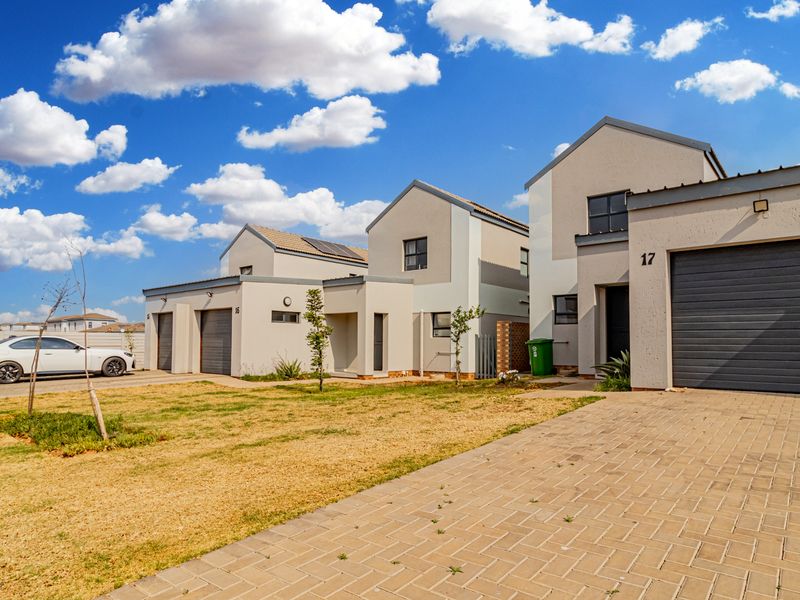 Front exterior view of modern townhouse units featuring paved driveways, sectional garage doors, and a shared residential street frontage.