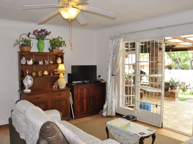 A living room featuring laminate flooring, a ceiling fan, and direct access through a security gate to a covered outdoor patio area.