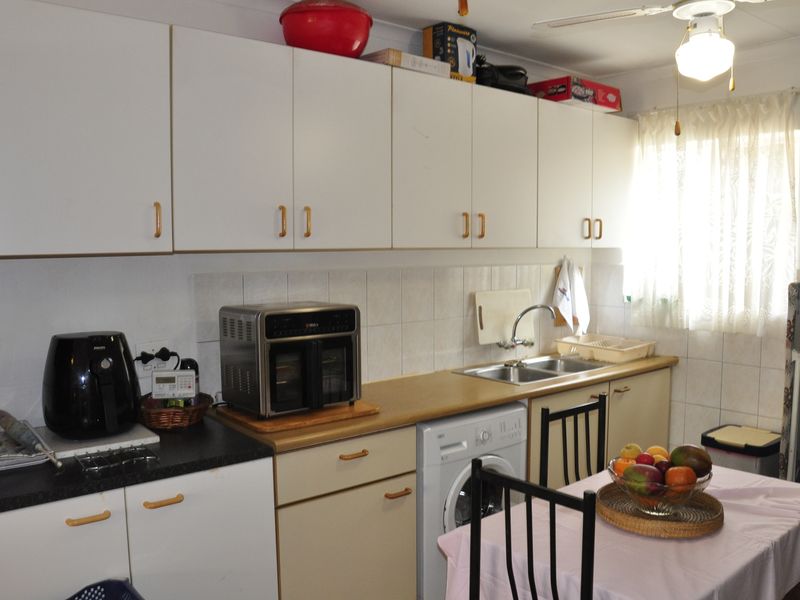 A functional kitchen featuring white cabinetry, laminate countertops, a double bowl sink, tiled splashback, and an integrated washing machine.