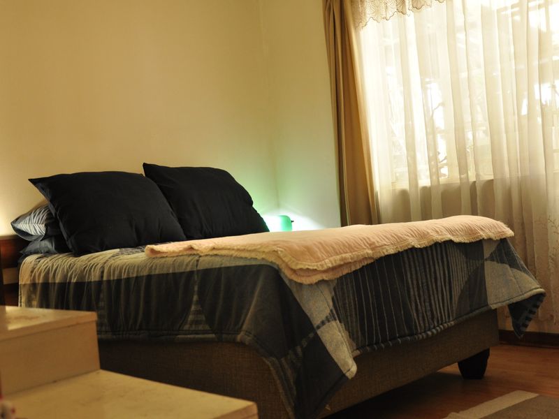 A cozy bedroom featuring laminate flooring and natural light filtering through window curtains.