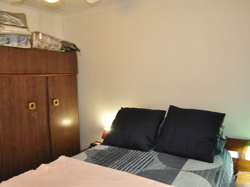 A functional bedroom featuring a built-in wooden wardrobe and a ceiling fan, providing essential storage and climate control.