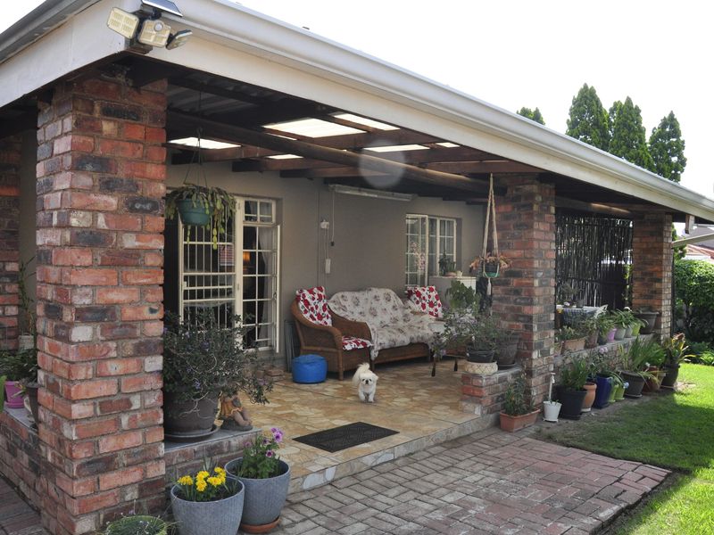 A covered patio area featuring exposed brick pillars, a timber pergola roof with translucent panels, and tiled flooring, providing a functional outdoor living space.