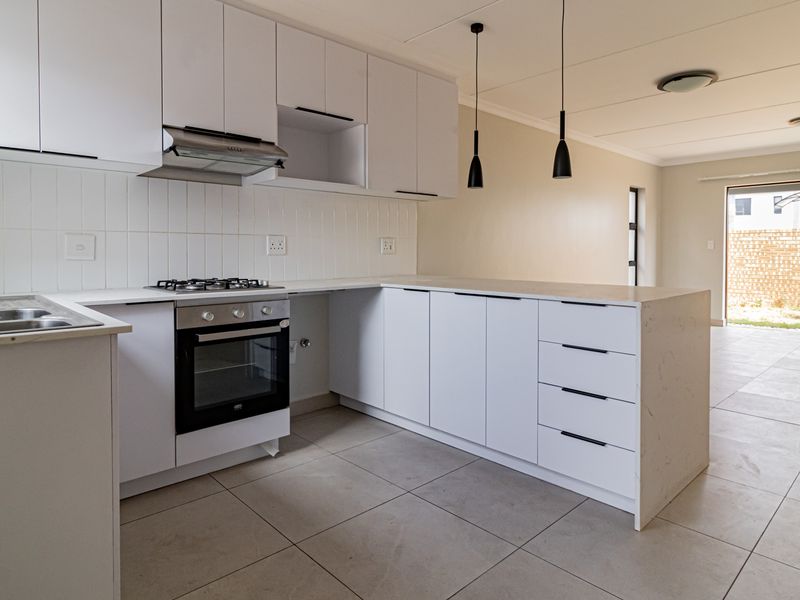 Modern open-plan kitchen featuring white cabinetry, gas hob, oven, and tiled flooring, flowing seamlessly into a bright living area with sliding door access.