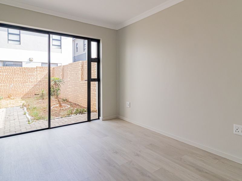 A bright, empty bedroom featuring modern laminate flooring, neutral walls, and a large sliding glass door providing direct access to the rear garden.