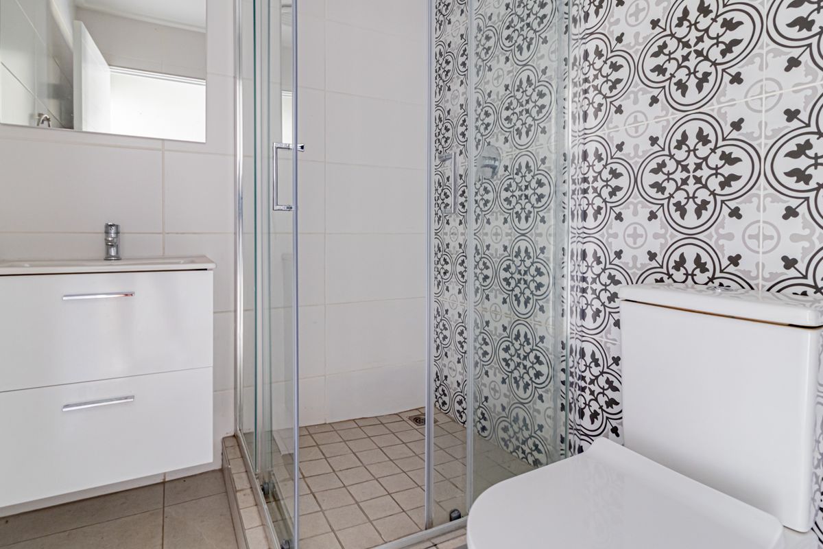 A clean, modern bathroom featuring a glass shower enclosure, vanity cabinet with basin, and decorative patterned wall tiles.