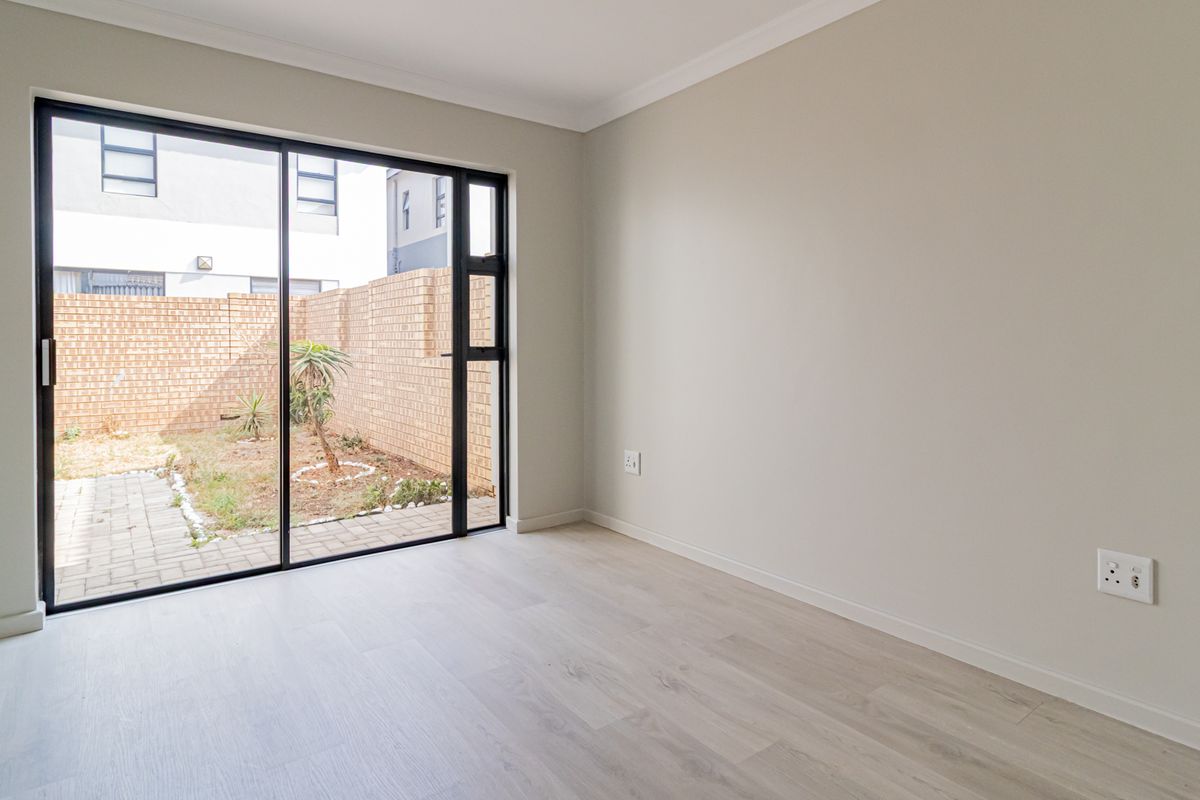 A bright, empty bedroom featuring modern laminate flooring, neutral walls, and a large sliding glass door providing direct access to the rear garden.