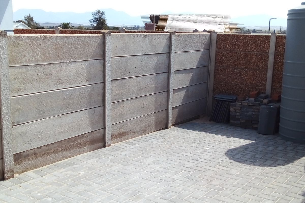A rear outdoor area featuring paved flooring, a precast concrete boundary wall, and a large water storage tank.