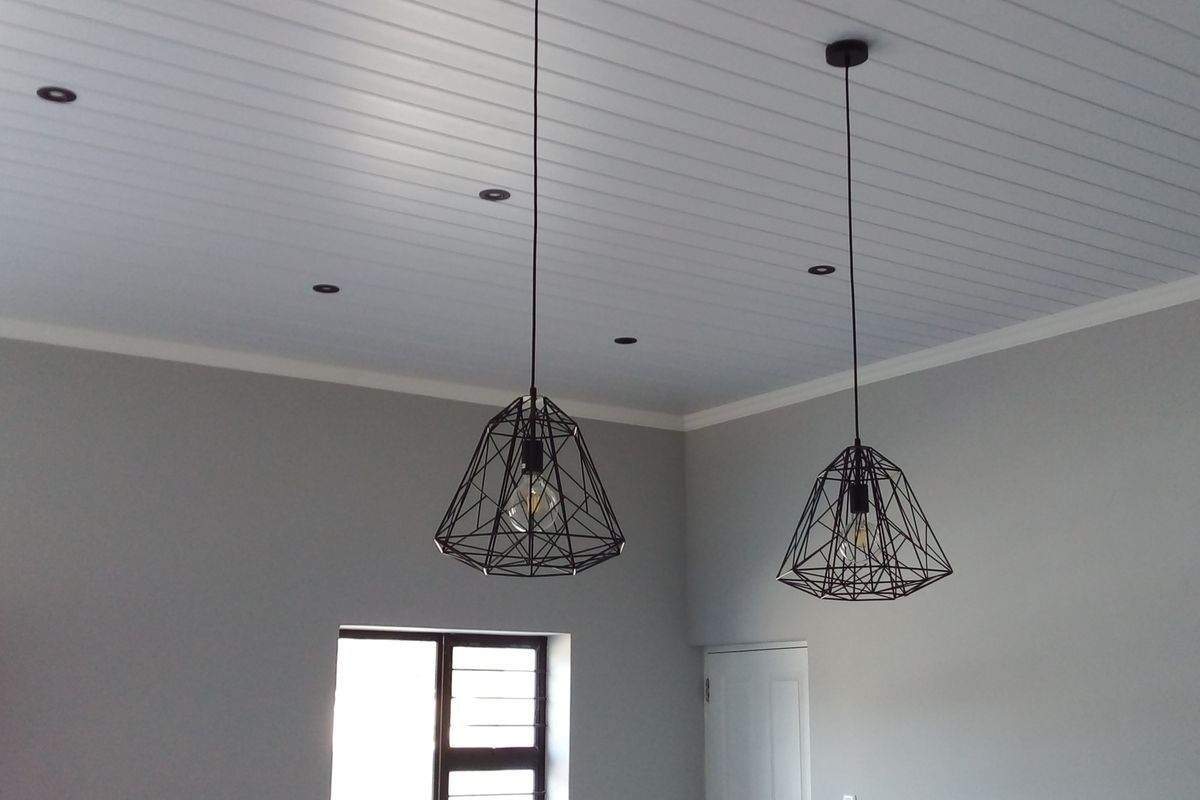 A bright, empty living area featuring a modern tongue and groove ceiling, recessed downlights, and stylish geometric pendant lighting.