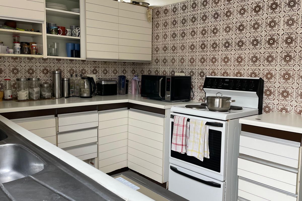 A dated kitchen featuring white cabinetry, a freestanding stove, and patterned wall tiles, offering a functional layout with ample counter space.