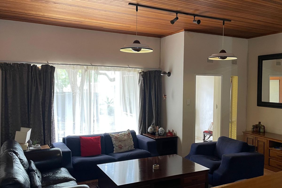 Spacious living room featuring a warm timber-paneled ceiling, track lighting, and large windows that provide ample natural light.