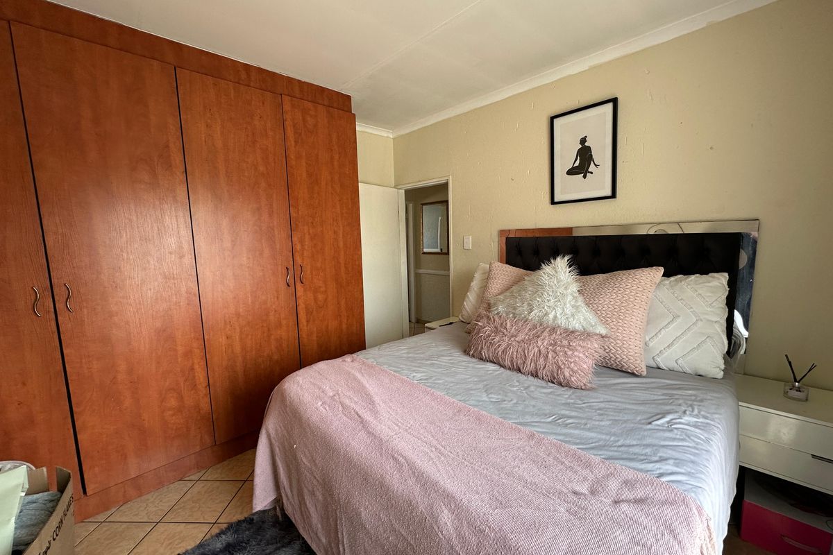 A bedroom featuring built-in wooden cupboards, tiled flooring, and coved ceilings, offering a functional space with potential for cosmetic updates.
