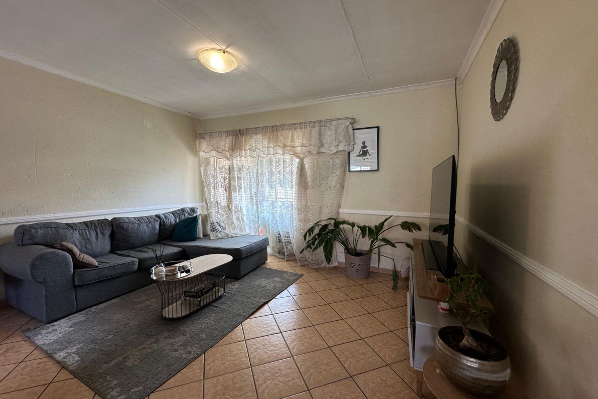 A living room featuring tiled flooring, chair rail molding, and a ceiling light fixture, with visible wear on the wall surfaces.